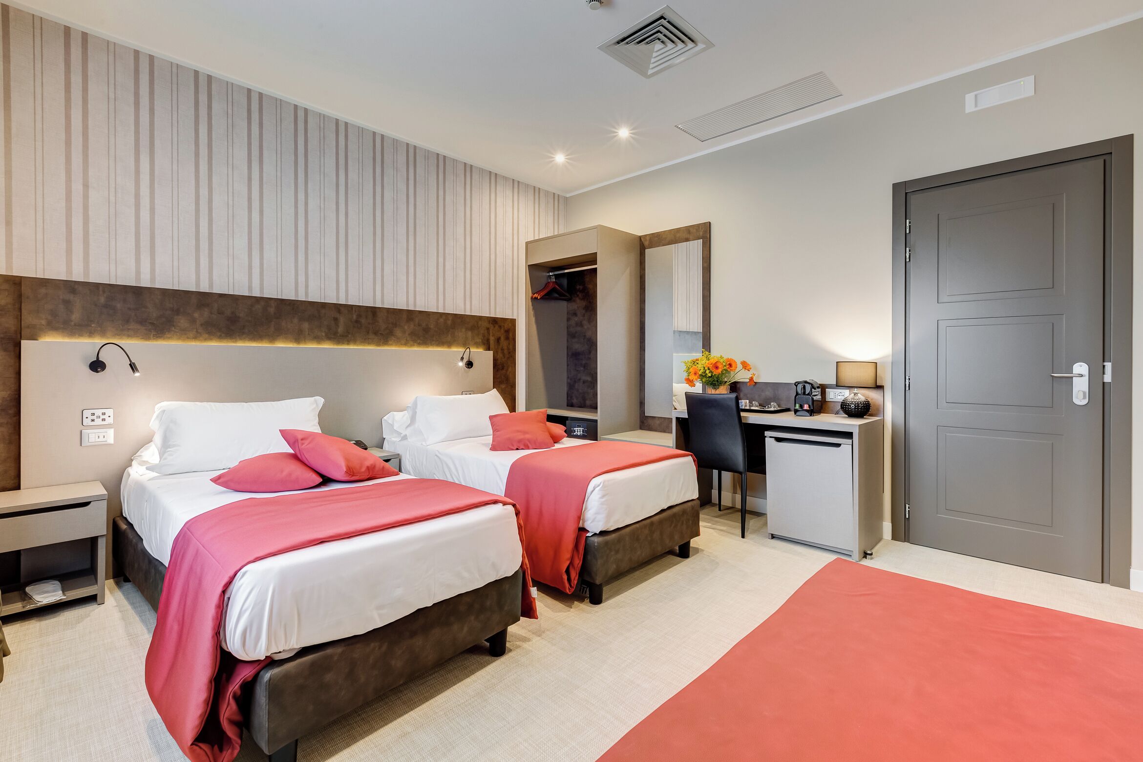 A hotel room with two beds, a desk, a wardrobe, and a door.