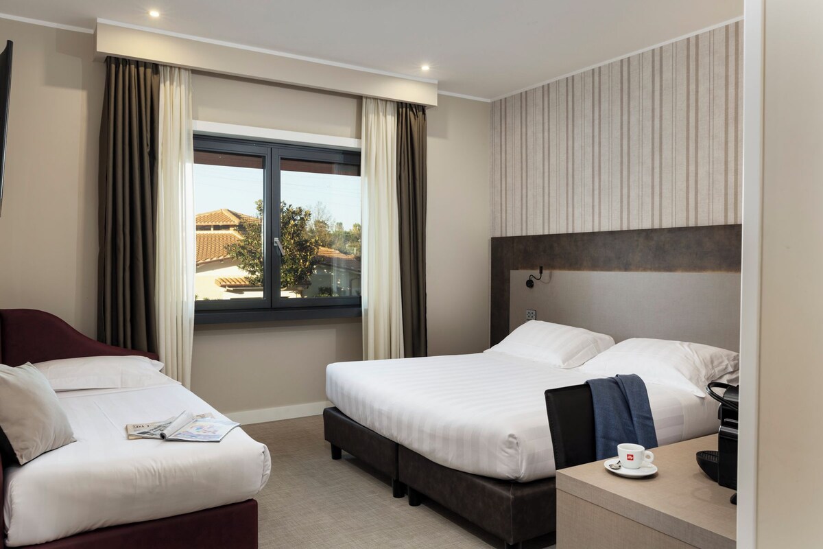 A hotel room with two beds, a desk, and a window with curtains.