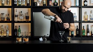 Un bartender preparando una bebida en la barra, con estantes llenos de botellas de licor al fondo.