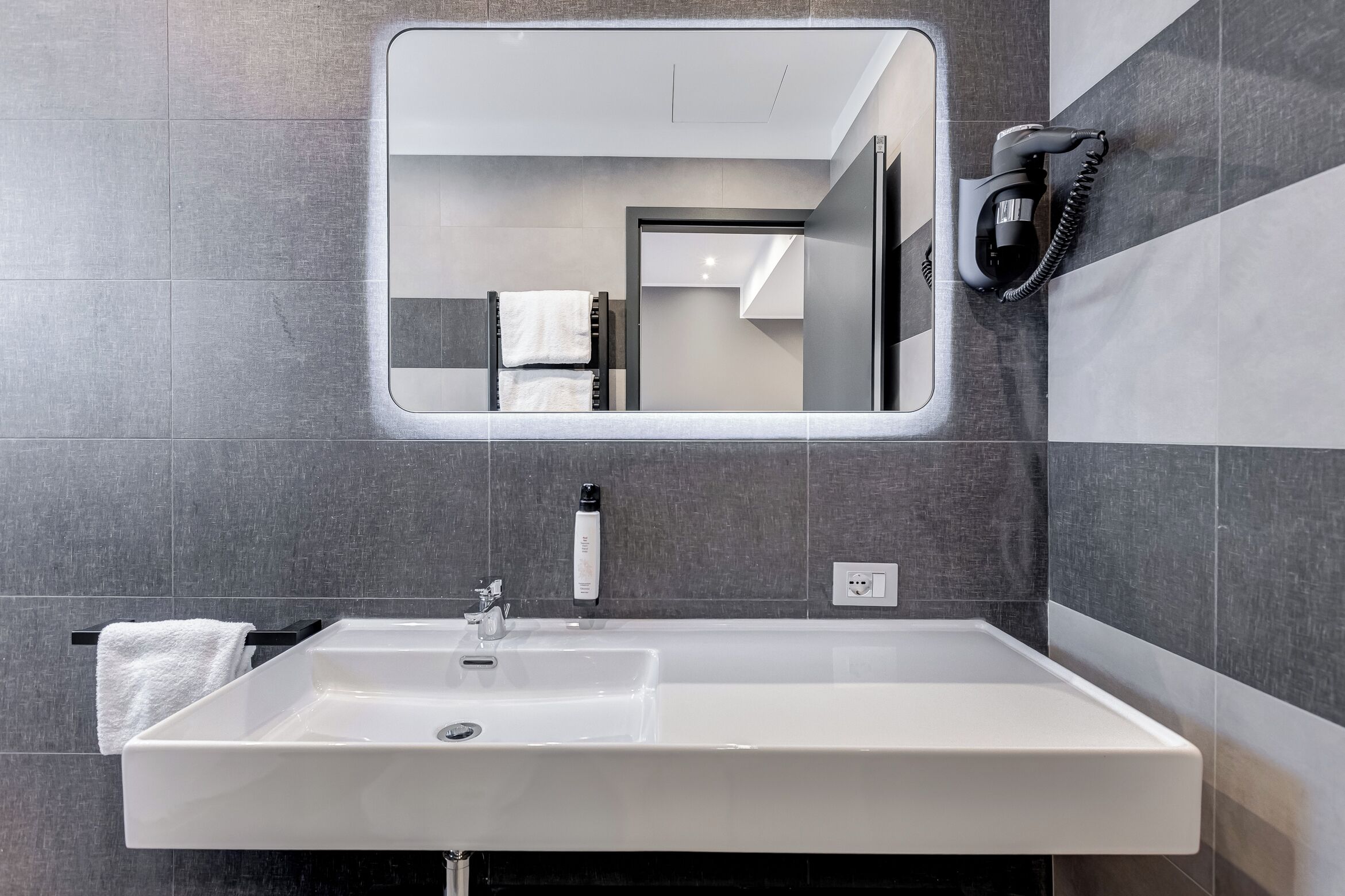 A modern bathroom with a large rectangular sink, a mirror, and a towel rack.
