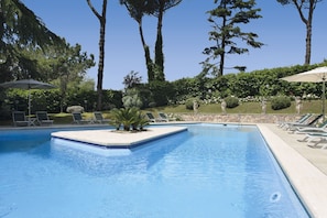 A swimming pool with lounge chairs and umbrellas, surrounded by trees and a stone wall.