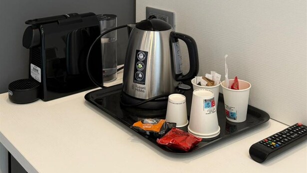 Een dienblad met een koffiezetapparaat, bekers, een afstandsbediening en snacks in een hotelkamer.