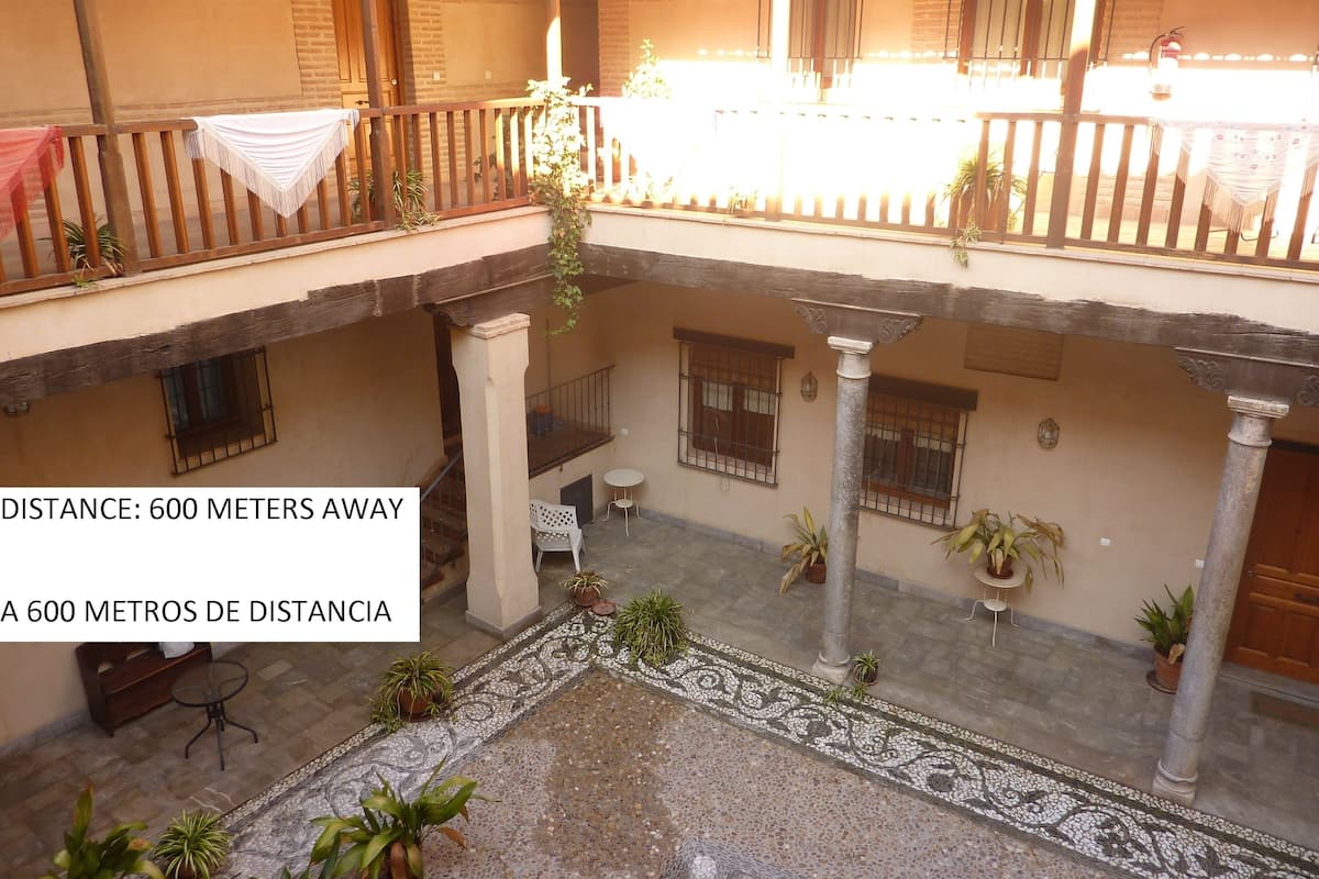 A courtyard with a tiled floor, potted plants, and a wooden balcony railing.