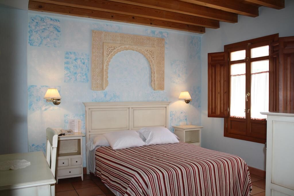 A bedroom with a bed, bedside lamps, a nightstand, a wardrobe, and a window with wooden shutters.
