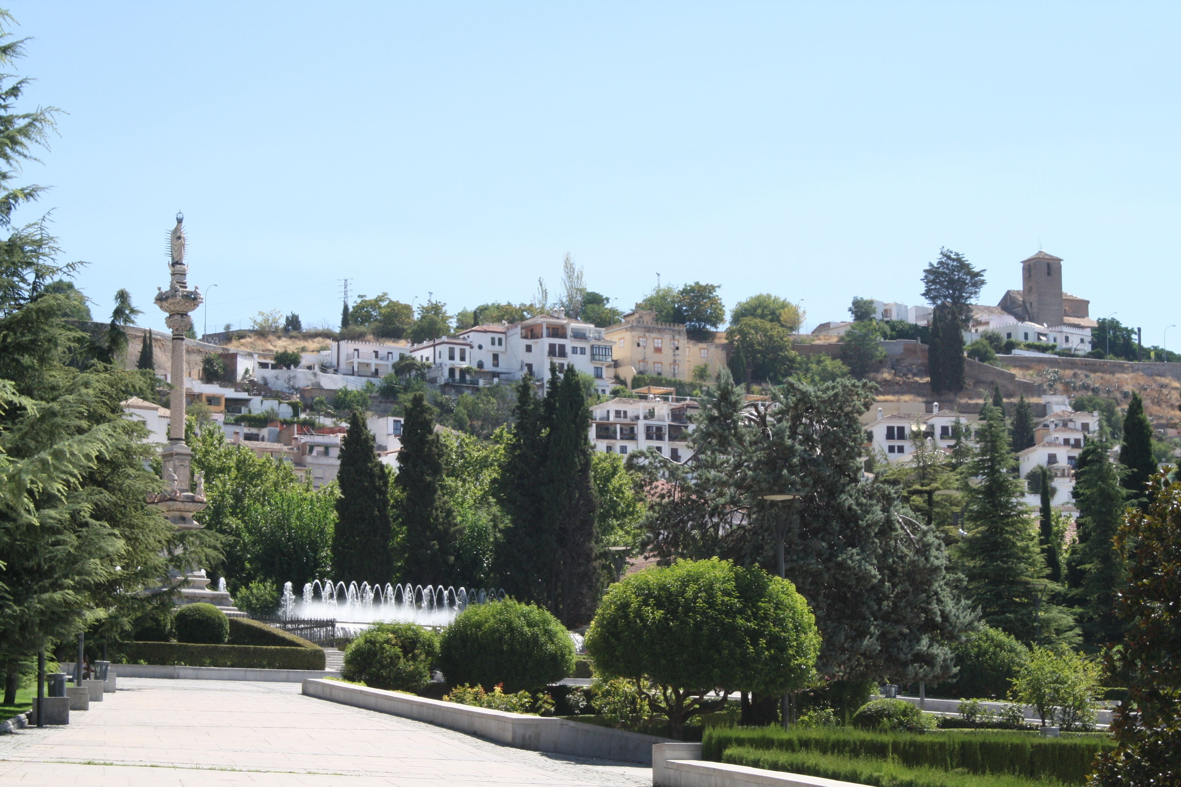 A hillside town with historic buildings, a fountain, and well-maintained gardens.