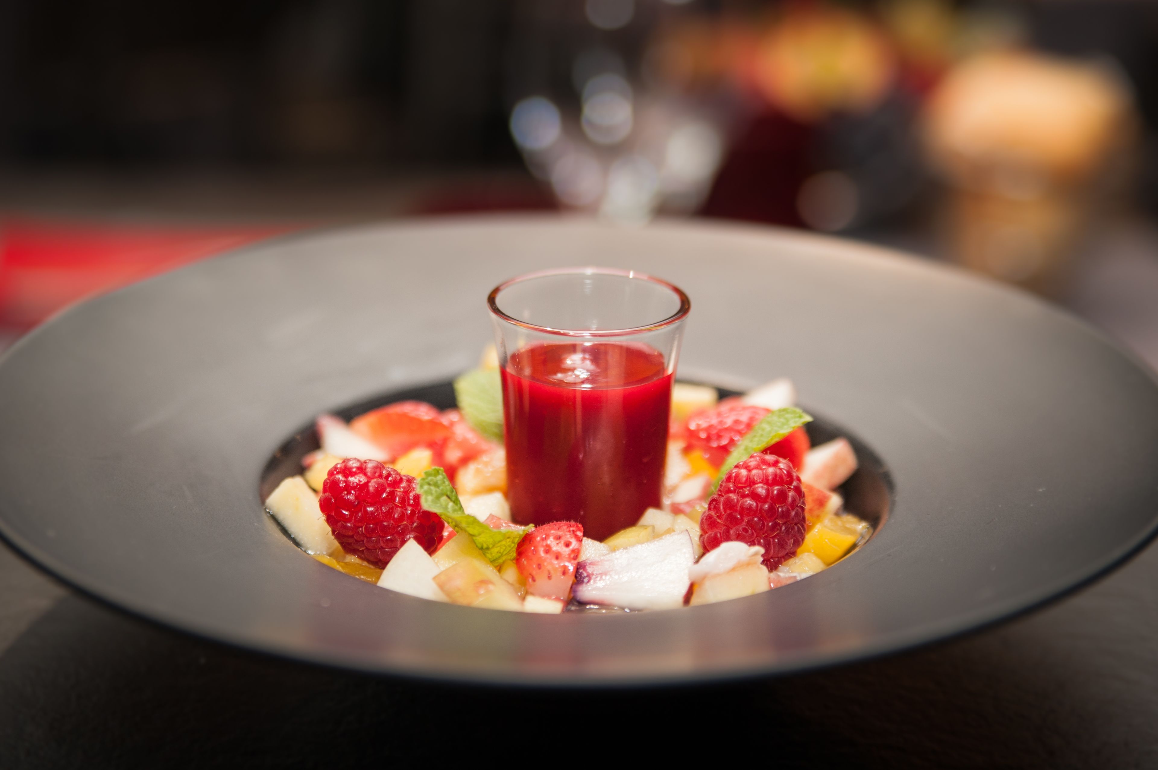 Un plato de postre con una copa de líquido rojo, fresas y otras frutas.