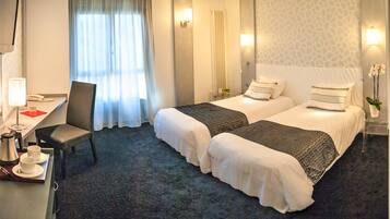 Camera d'albergo con due letti, una scrivania con una sedia, una macchina per il caffè e un vaso con fiori.