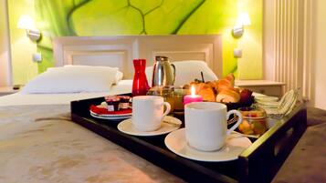 A neatly arranged breakfast tray on a bed with white linens, a red vase, a silver pitcher, and a variety of pastries.
