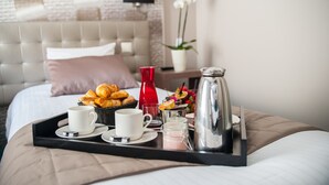 A neatly arranged breakfast tray on a bed with croissants, a red bottle, a coffee pot, and a fruit bowl.