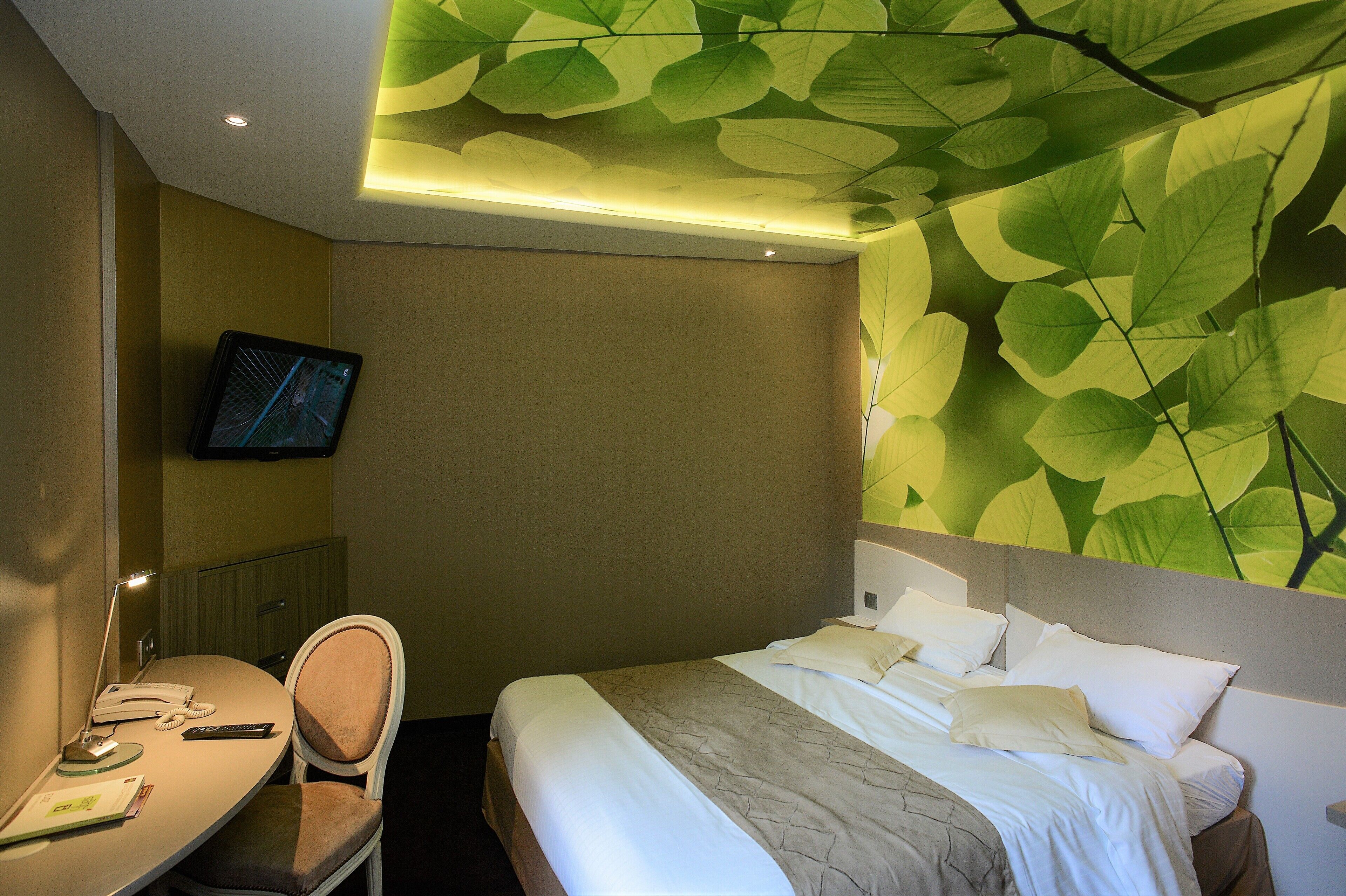 A hotel room with a bed, a desk, a chair, a television, and a wall with a leaf pattern.