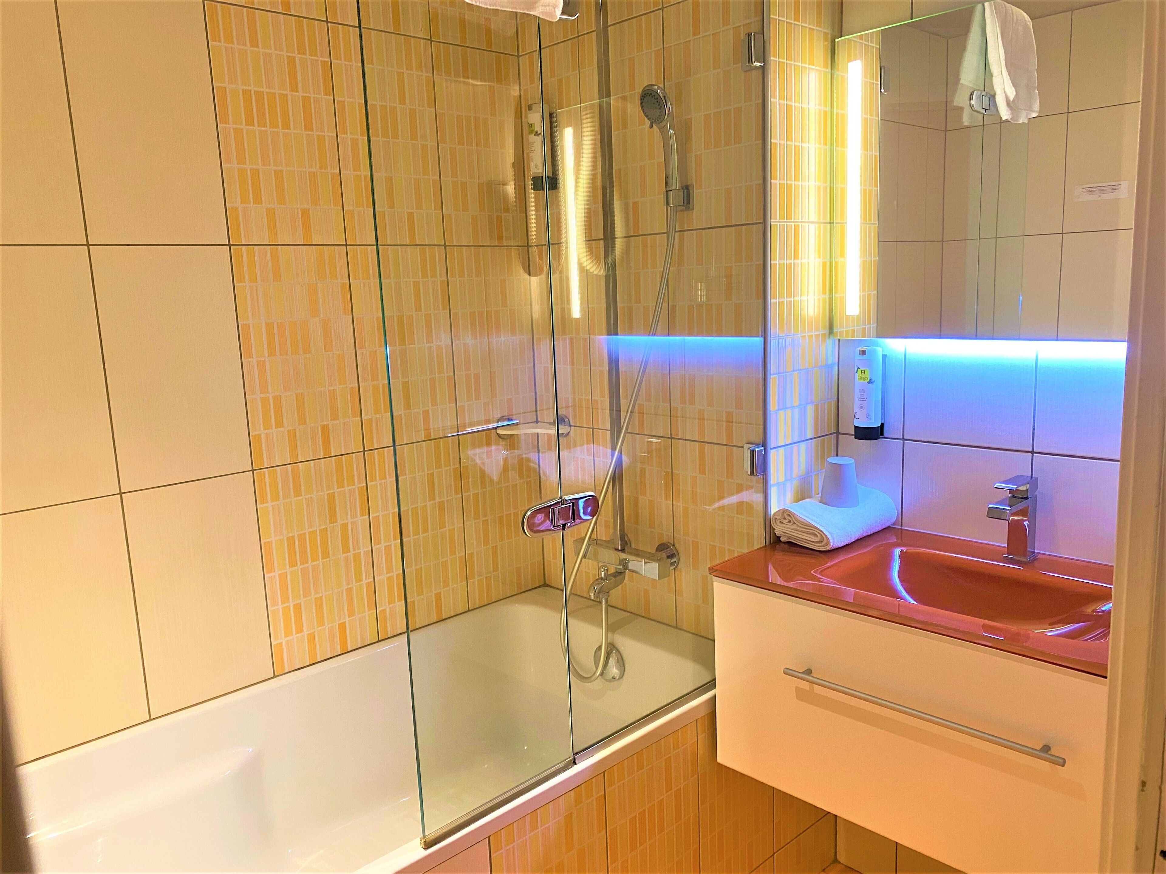Un baño con cabina de ducha de vidrio, un lavabo blanco y un espejo.