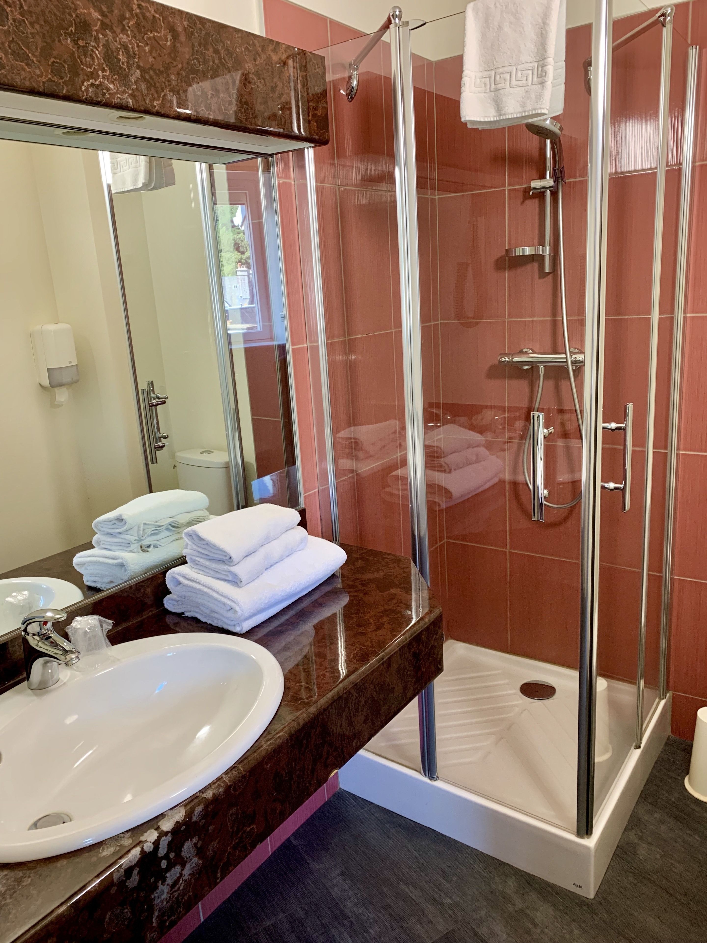 A bathroom with a glass-enclosed shower, a sink, a mirror, and neatly stacked towels.