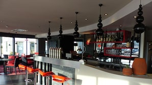 A modern bar area with red and black bar stools, a counter with a wine rack, and pendant lighting.
