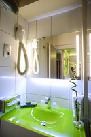 Un baño con un lavabo verde, un secador de pelo y un espejo que refleja a alguien tomando una fotografía.