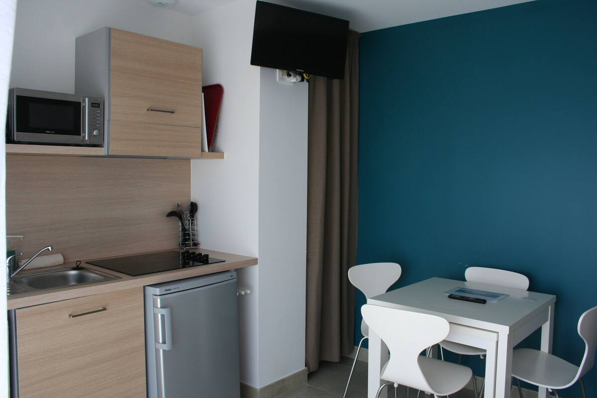 A compact kitchen with a microwave, sink, and a small refrigerator. There is a dining area with a table and chairs.