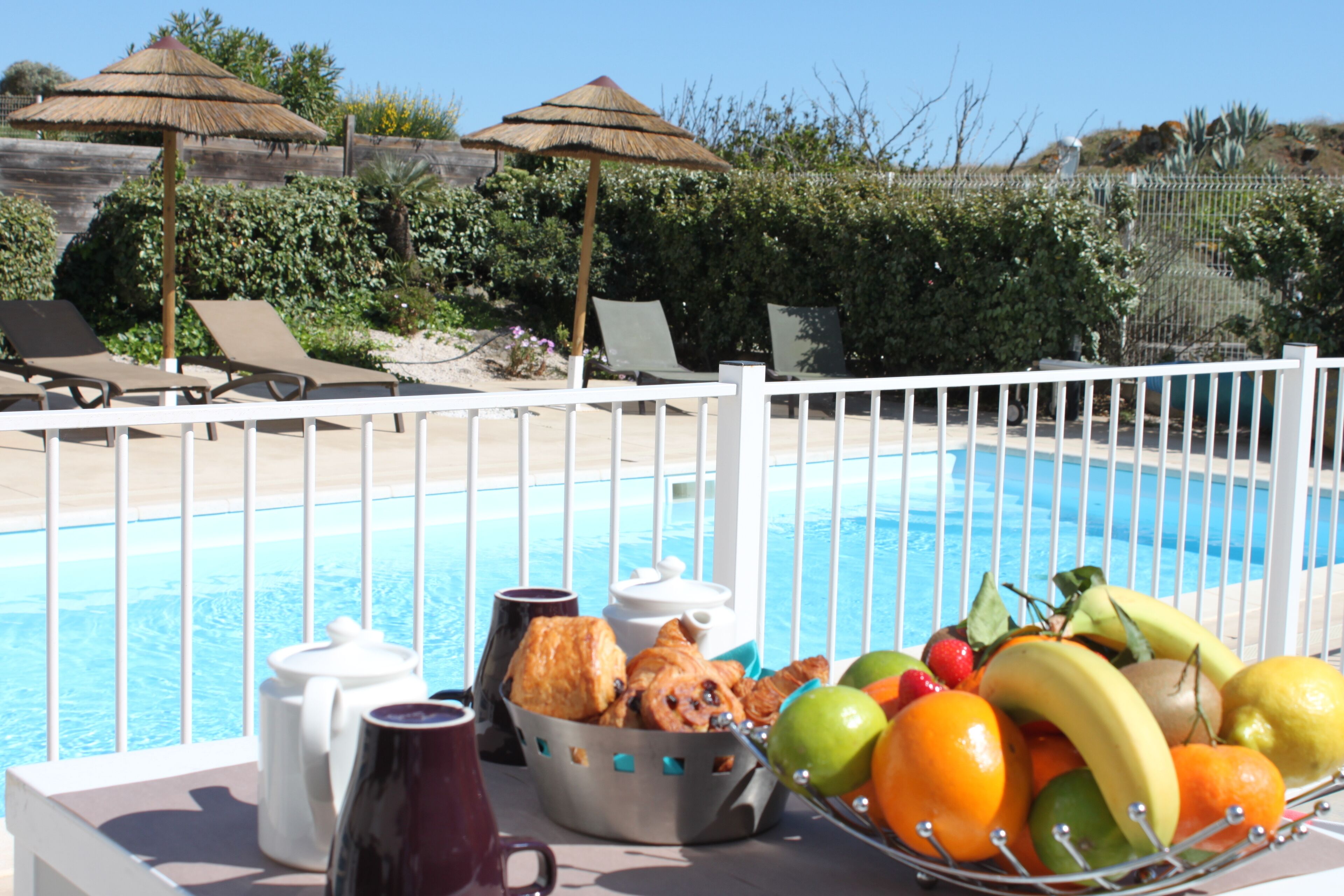 A poolside table with a fruit basket, a coffee pot, and a mug.
