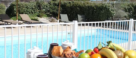 A poolside table with a fruit basket, a coffee pot, and a mug.