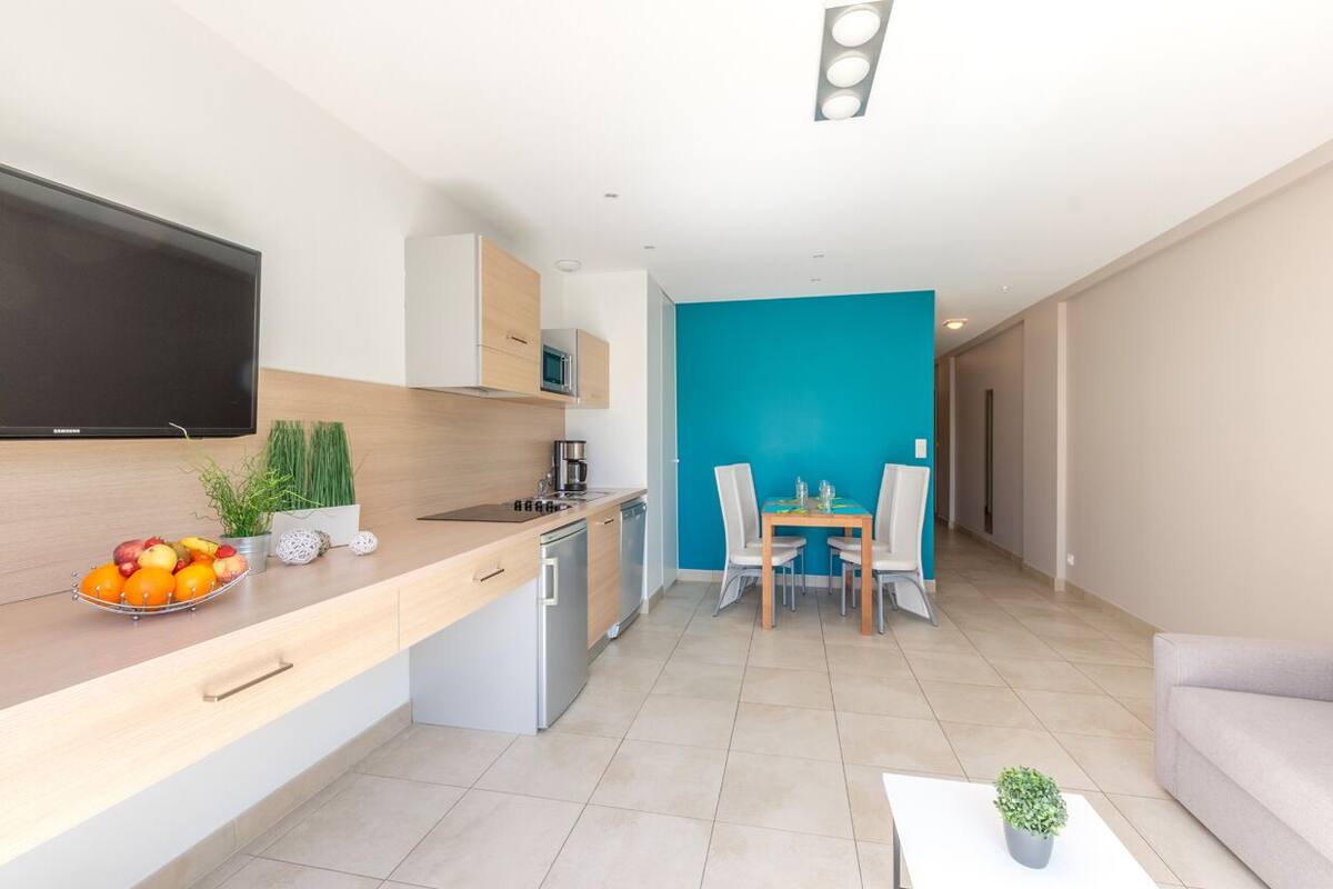 A modern kitchen with a flat-screen TV, a dining area with a table and chairs, and a living room with a sofa.