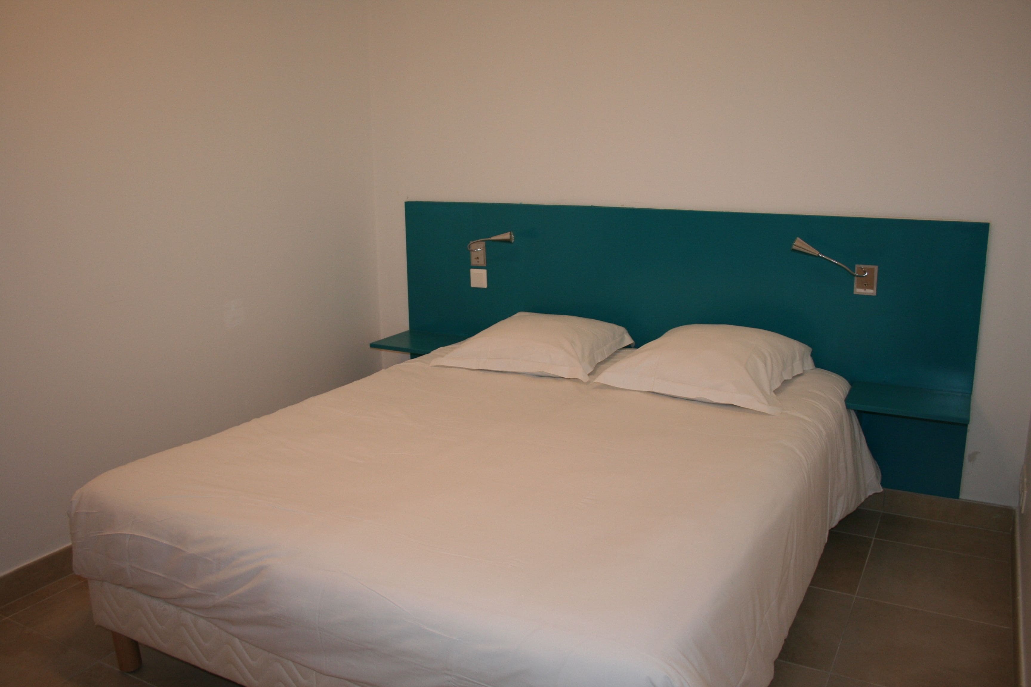 A single bed with a teal headboard, white bedding, and two bedside tables with lamps.