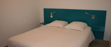 A single bed with a teal headboard, white bedding, and two bedside tables with lamps.