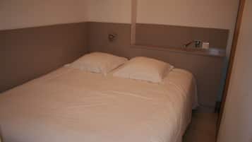 Una cama pequeña y bien hecha en una habitación compacta, con cabecera y repisa superior.