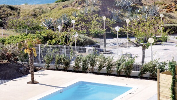 A pool area with a clear view of the ocean, surrounded by a fence and various plants. - Thalacap Résidence (Agde)