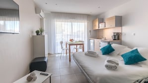 A modern hotel room with a bed, a desk, a chair, a small table, and a kitchenette. - Thalacap Résidence (Agde)
