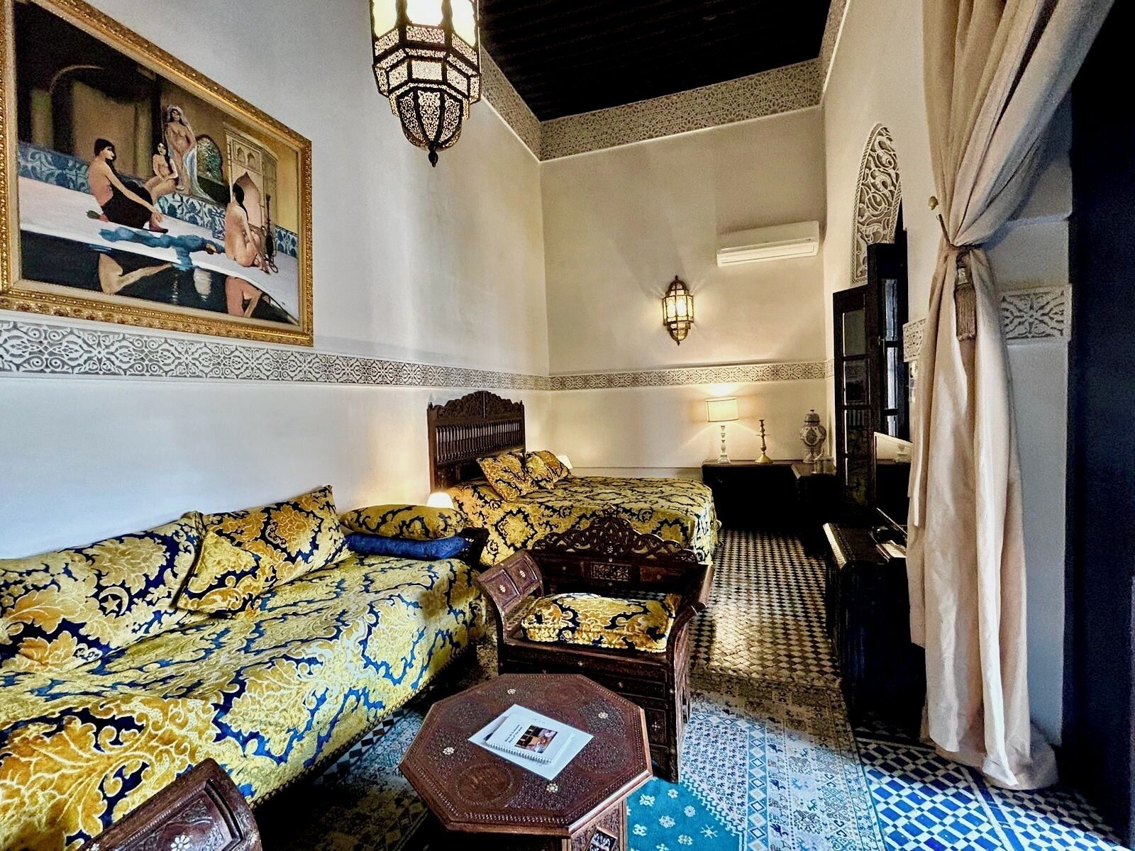 Une pièce de style marocain traditionnel, avec des canapés à motifs, une table basse en bois, un tableau et un sol carrelé.