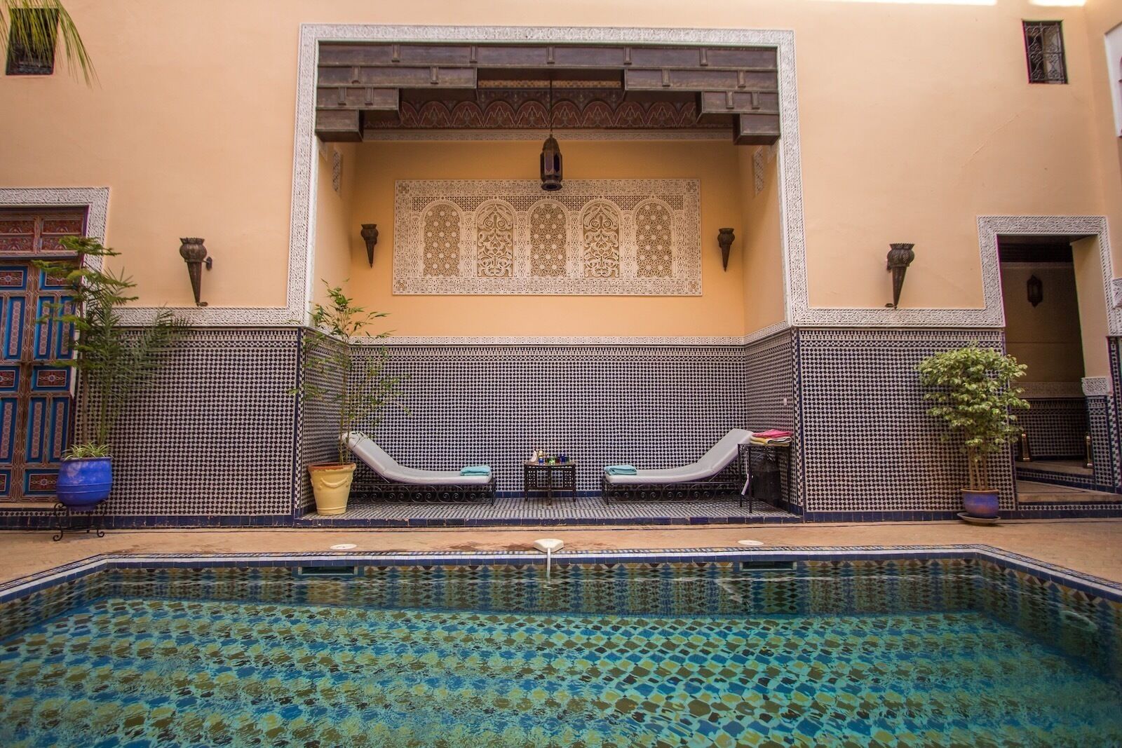 A pool area with a tiled floor, two lounge chairs, and a decorative wall with intricate patterns.