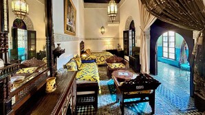 A traditional Moroccan room with a bed, a wooden table, a mirror, and a view of the outside.