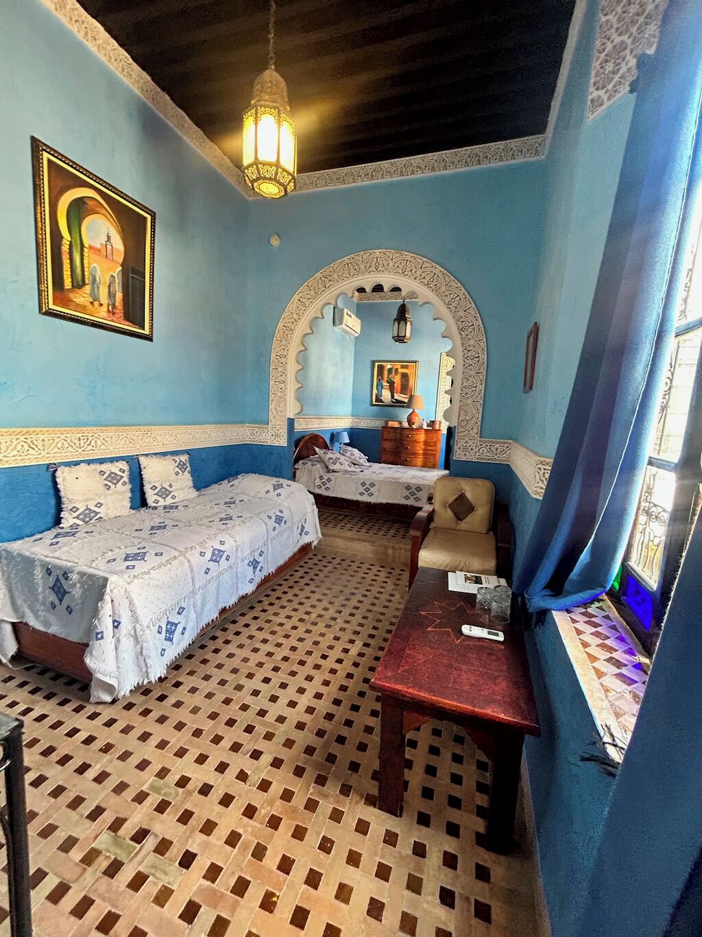 Une pièce avec un sol à motifs, un lit recouvert d’une couvre-lit à motifs, un canapé, une petite table et une lampe fixée au mur.