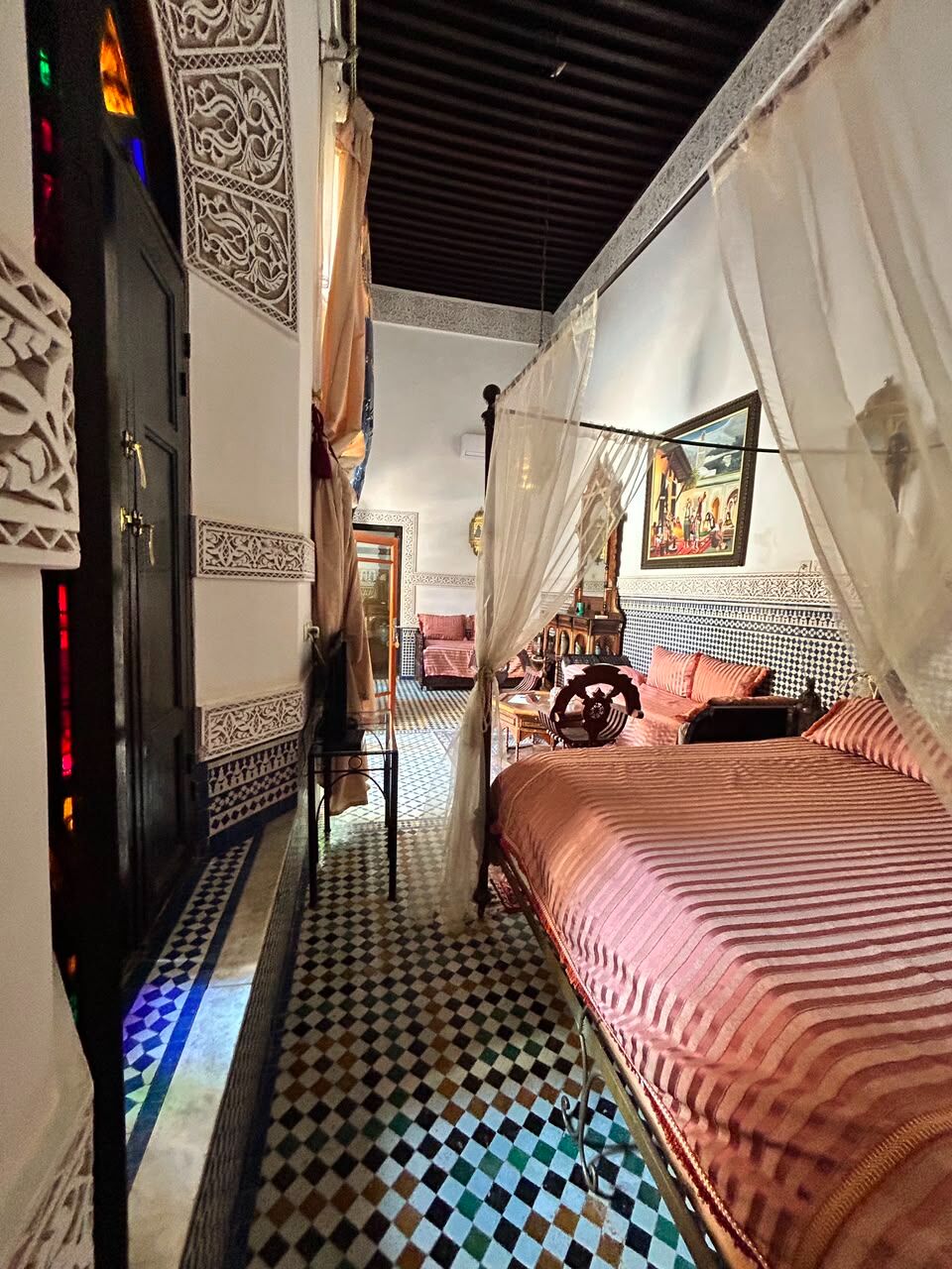 Una habitación con piso a cuadros, cama con colcha a rayas, una silla y una pared decorativa.