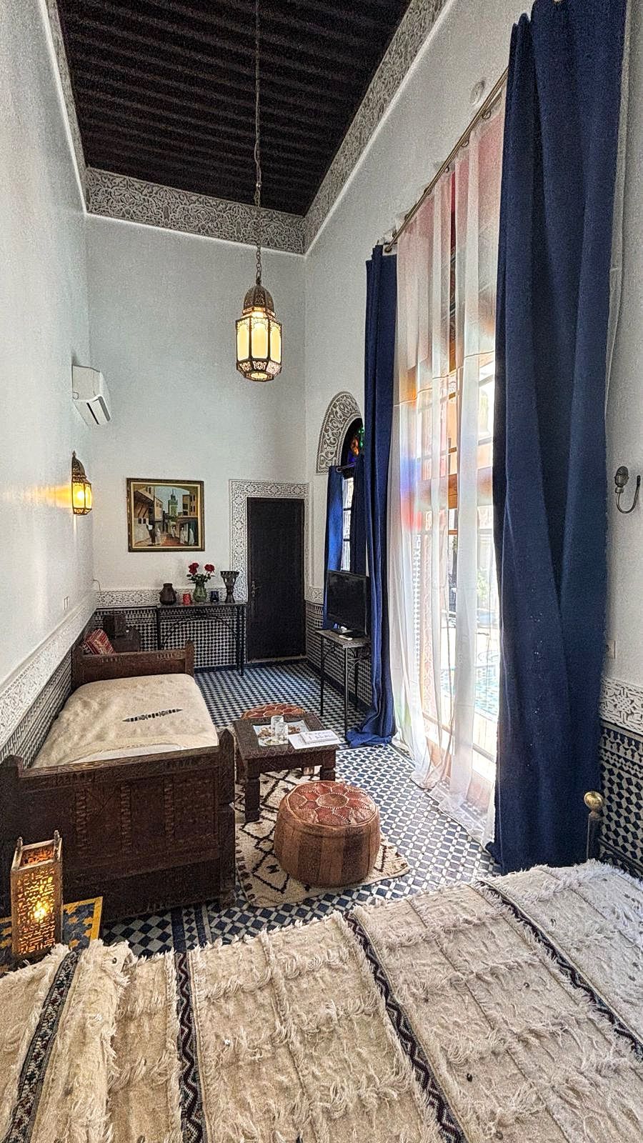 Quarto com chão xadrez, uma cama, um sofá, uma mesa pequena, uma televisão e um arco decorativo.