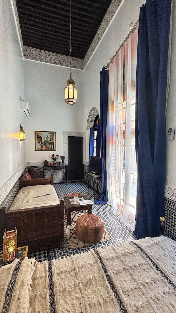 A room with a checkered floor, a bed, a sofa, a small table, a television, and a decorative archway. - Riad Fes Baraka Piscine & Spa (Fes)