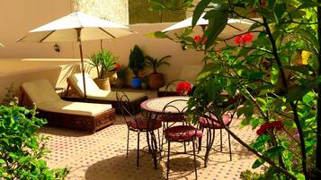 A sunlit outdoor seating area with a tiled floor, lounge chairs, and umbrellas.