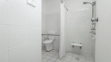 Un baño con azulejos blancos, un inodoro, una ducha con cortina y un estante pequeño.