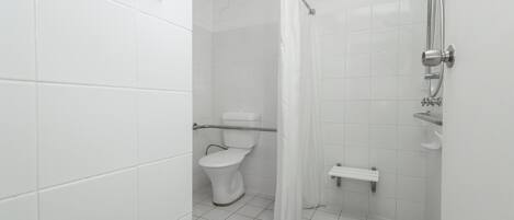 Un baño con azulejos blancos, un inodoro, una ducha con cortina y un estante pequeño.
