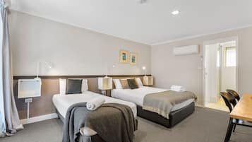 Habitación de hotel con dos camas, un escritorio y una silla. Hay lámparas de pared, una lámpara en el techo y un equipo de aire acondicionado.