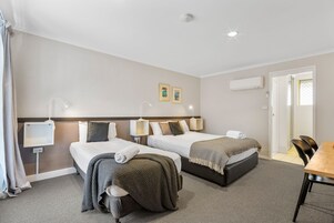 Habitación de hotel con dos camas, un escritorio y una silla. Hay lámparas de pared, una lámpara en el techo y un equipo de aire acondicionado.
