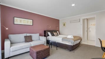 Une chambre d’hôtel avec un canapé gris, un lit recouvert d’une courtepointe à motifs, un petit pouf et un certificat encadré accroché au mur.