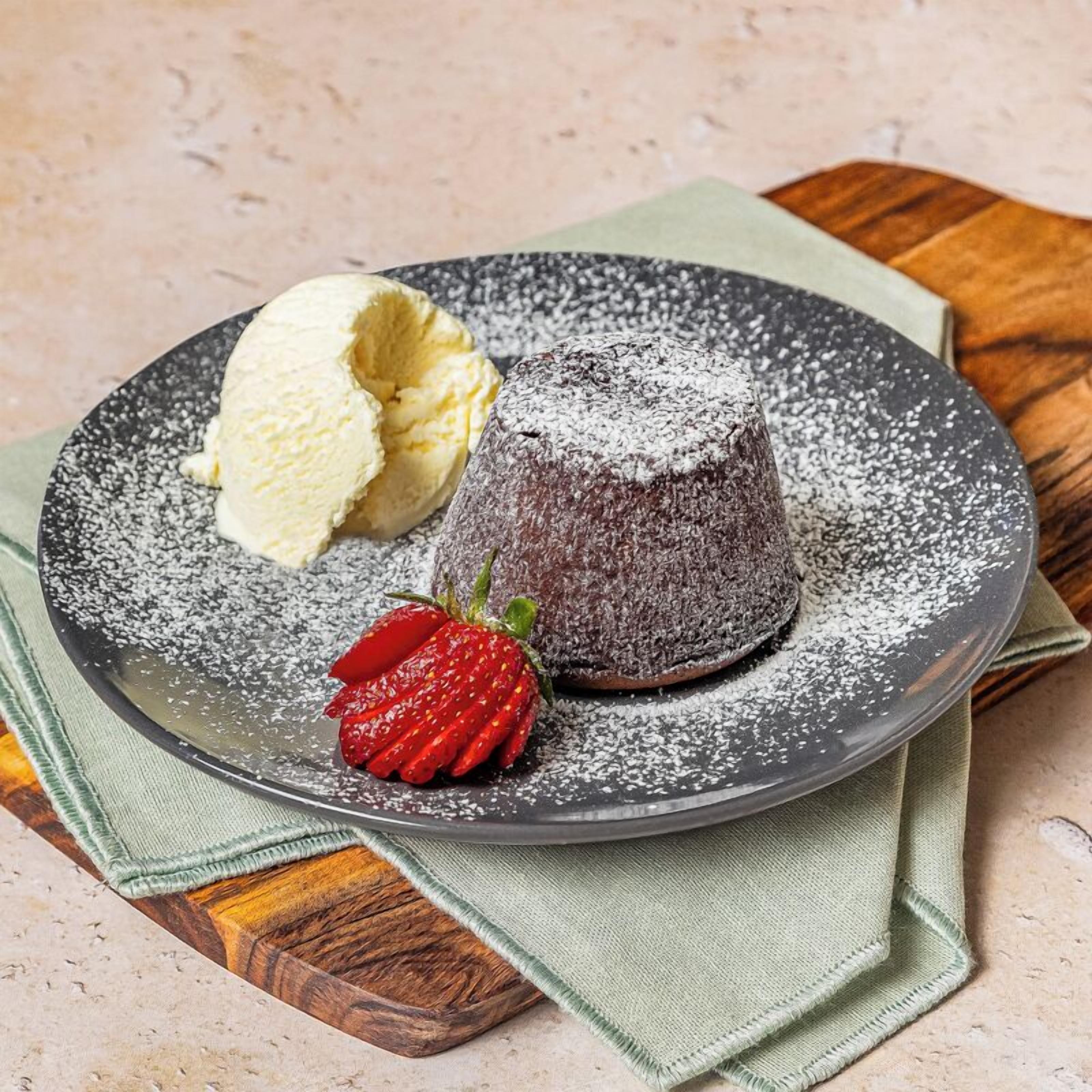 Ein Dessertteller mit einem Schokoladenlaufkuchen, einer Kugel Vanilleeis und einer Erdbeere.