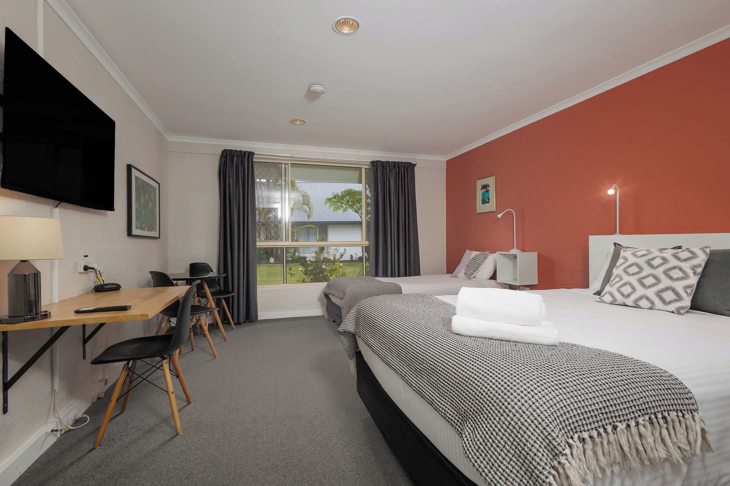 A hotel room with a bed, a desk, a chair, a TV, and a window with curtains.