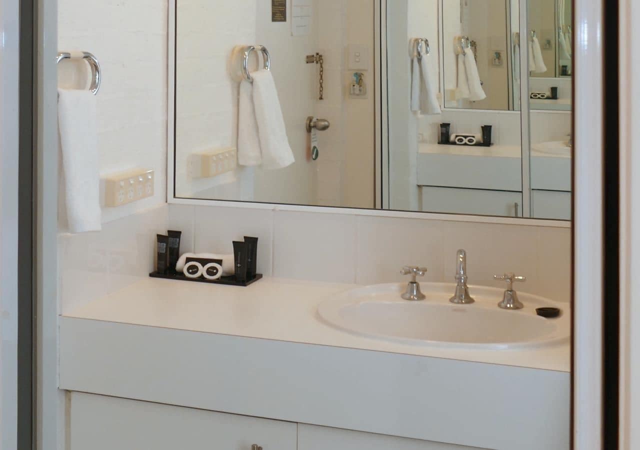 A bathroom with a white sink, two faucets, a mirror, and a towel rack.