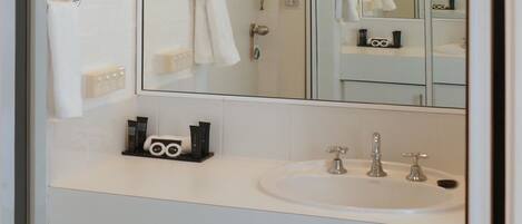 Un baño con un lavabo blanco, dos grifos, un espejo y un perchero para toallas.