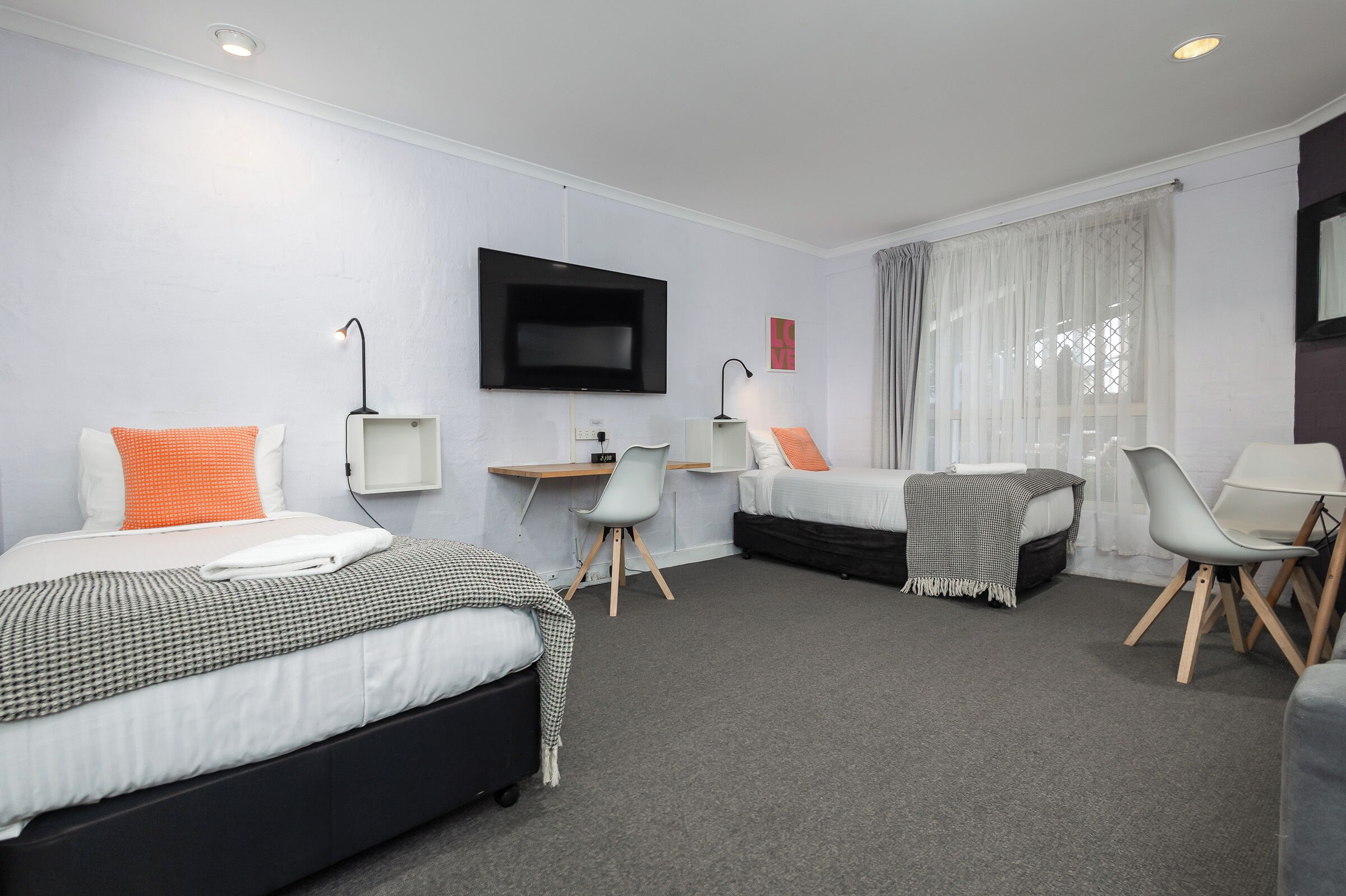 Une chambre d’hôtel avec deux lits, un bureau, une télévision et une fenêtre avec des rideaux.