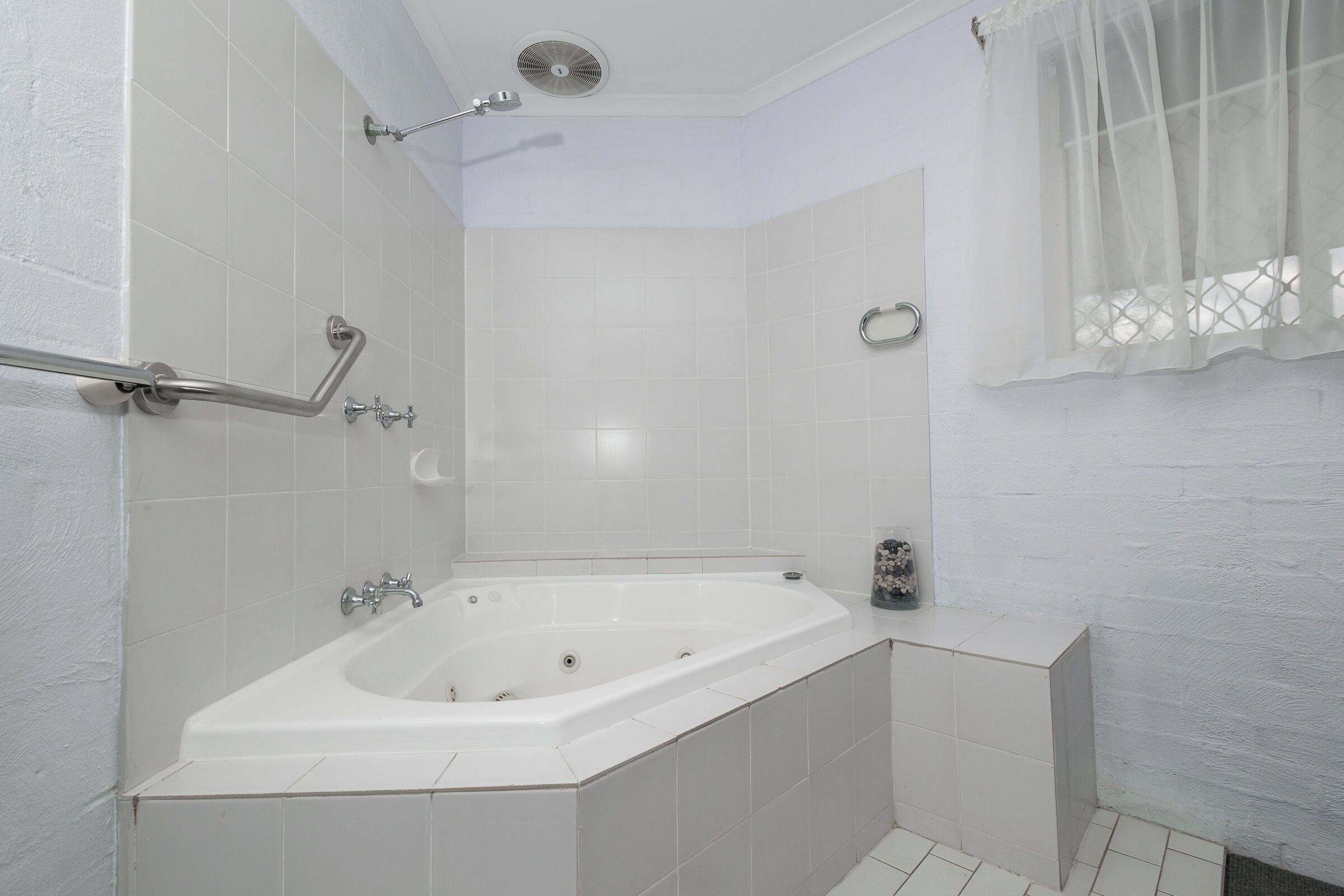 A modern bathroom with a freestanding bathtub, grab bars, a showerhead, and a window with a sheer curtain.