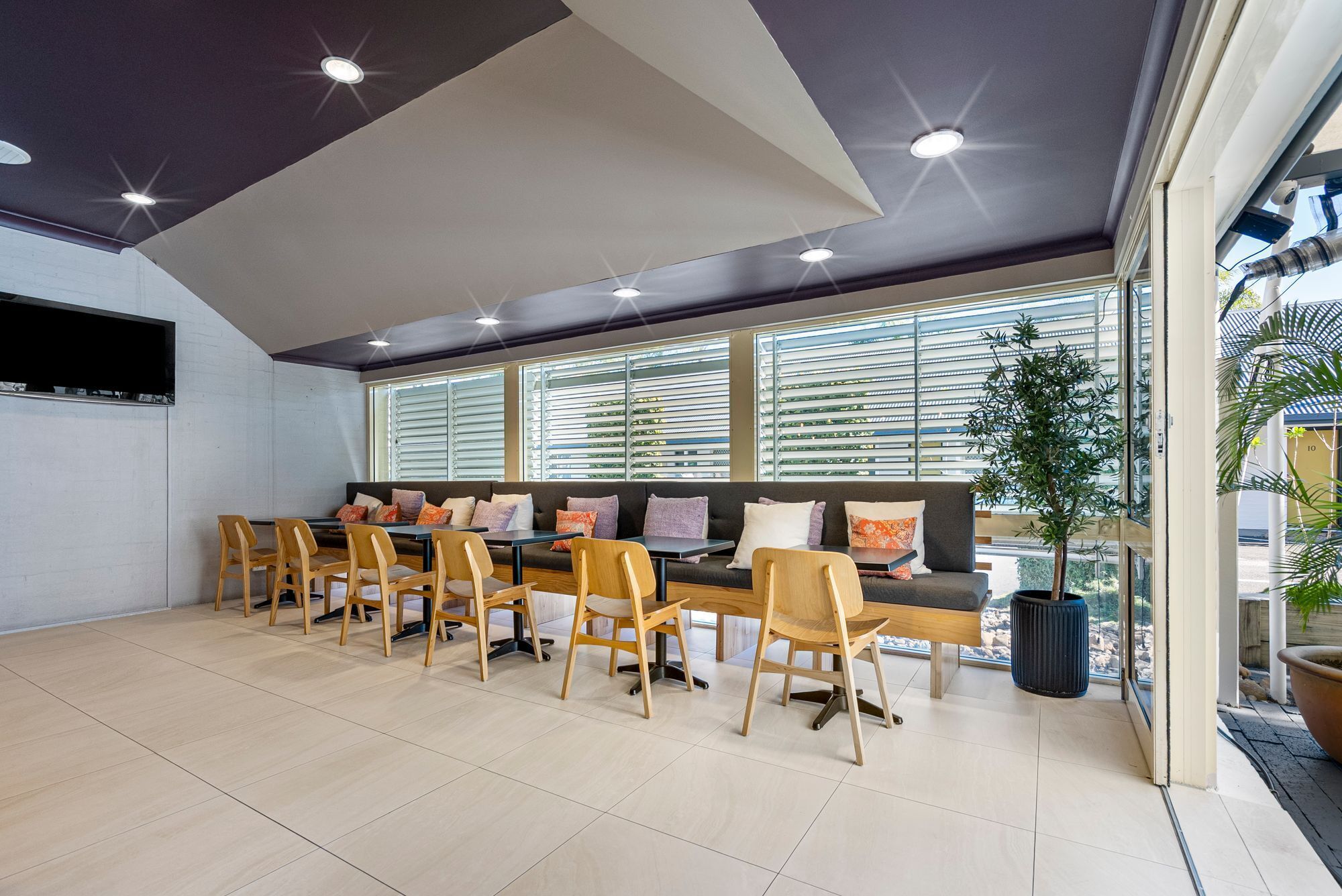 A modern meeting room with a long table, chairs, a sofa, and large windows with blinds.