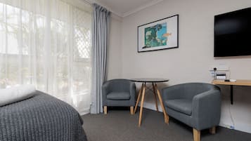Quarto de hotel com uma cama, duas poltronas, uma mesinha, televisão e um quadro na parede.