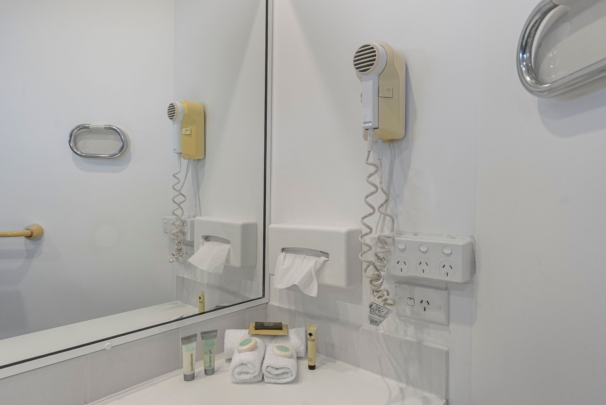 A bathroom with a mirror, a hairdryer, a towel rack, and toiletries on the counter.