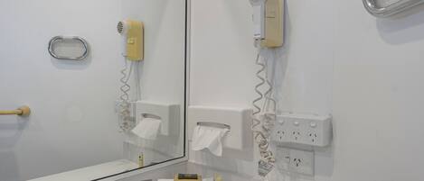 A bathroom with a mirror, a hairdryer, a towel rack, and toiletries on the counter.